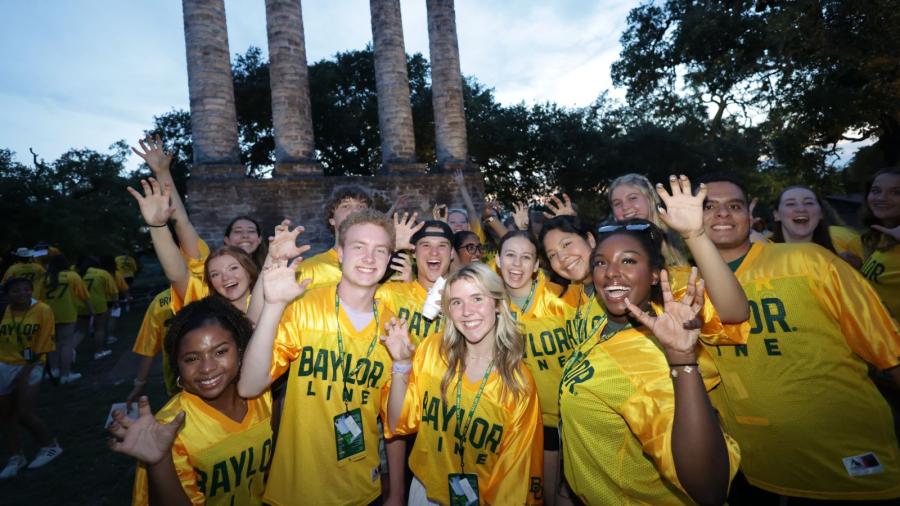 Baylor students wearing their gold Baylor Line jerseys do a bear claw with their hands with the four columns of Independence behind them