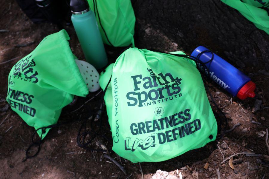 Green backpacks with the words Faith and Sports Institute, Greatness Defined.