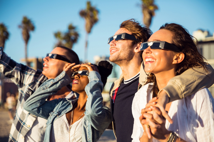 Friends wearing solar eclipse safety glasses look up at an eclipse of the sun.