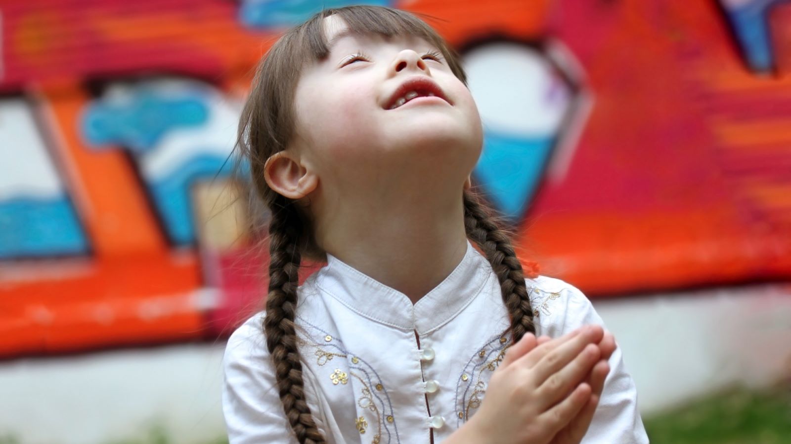 A child with Down Syndrome looks heavenward as she folds her hands in prayer