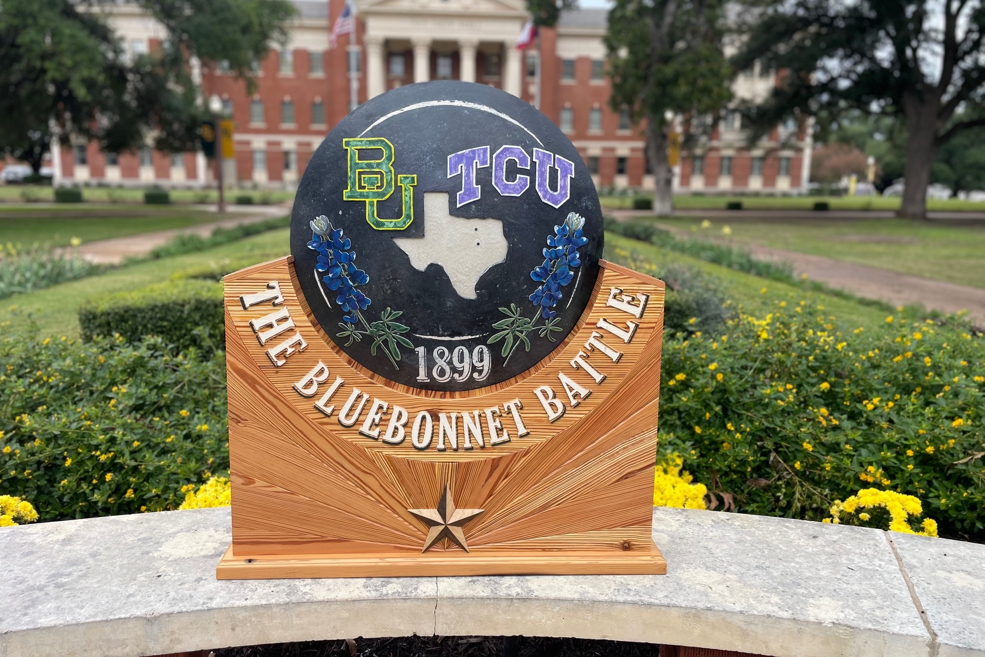 Bluebonnet Bowl trophy, a shield with BU, TCU, the state of Texas, bluebonnets and 1899, centered in a wooden stands that says The Bluebonnet Battle