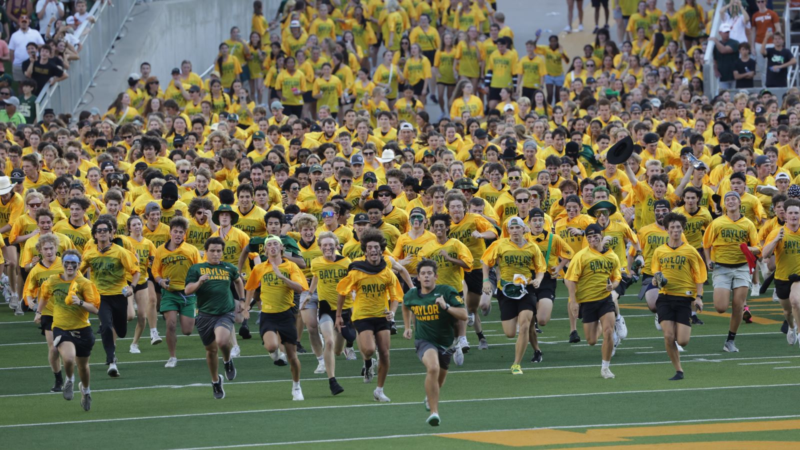 Baylor University freshman students run across the football field in their gold Baylor Line jerseys