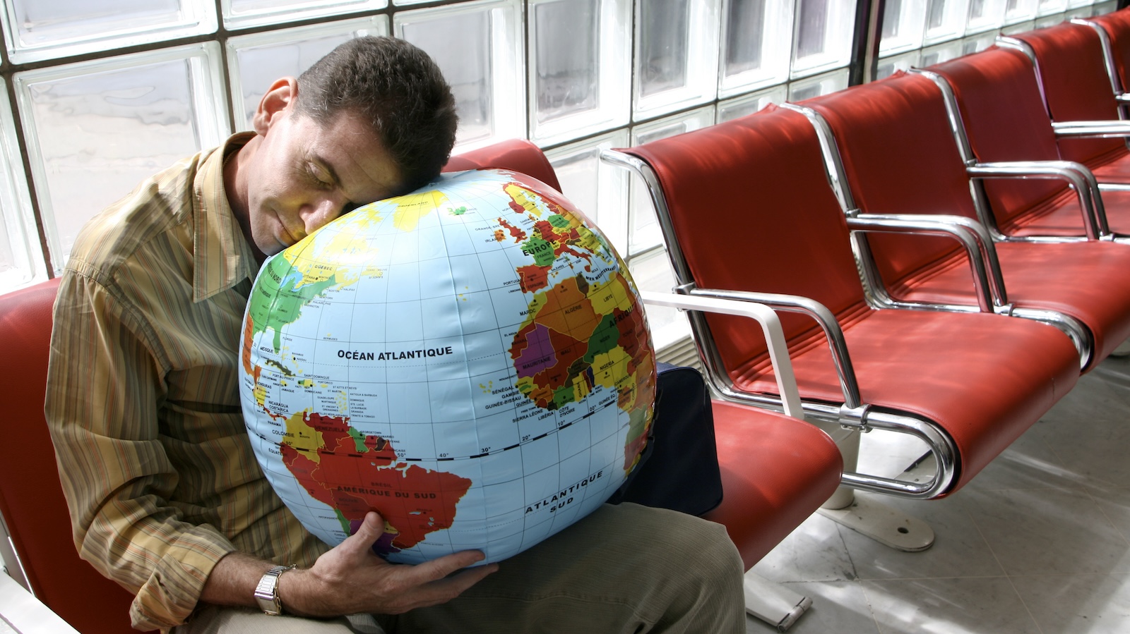 Man asleep on globe pillow at airport