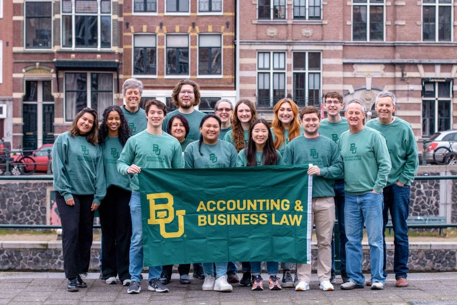 Baylor accounting students and faculty hold a green and gold Baylor pennant in front of the Youth With A Mission building in Amsterdam.