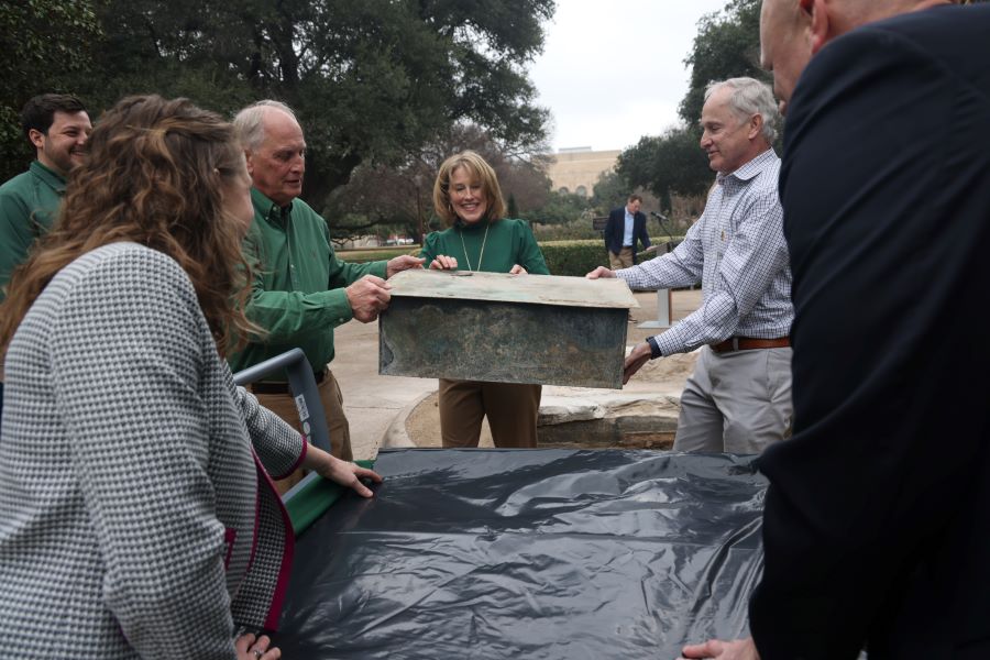 Three Collins Family members lift a large metal box - known as the Centennial Time Capsule at Baylor University - transferring it to a table for The Texas Collection.