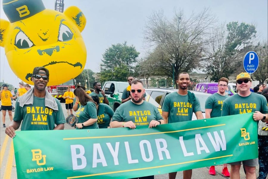 Law School students hold a green banner that says Baylor Law with a large Bear balloon in the background