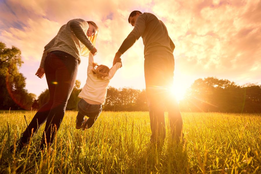 Happy family in the park at sunset. Mom and Dad hold the baby's hands.
