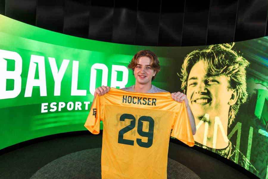 Colby "hockser" James hold a gold jersey with his name and number 29 with Baylor esports in the background.