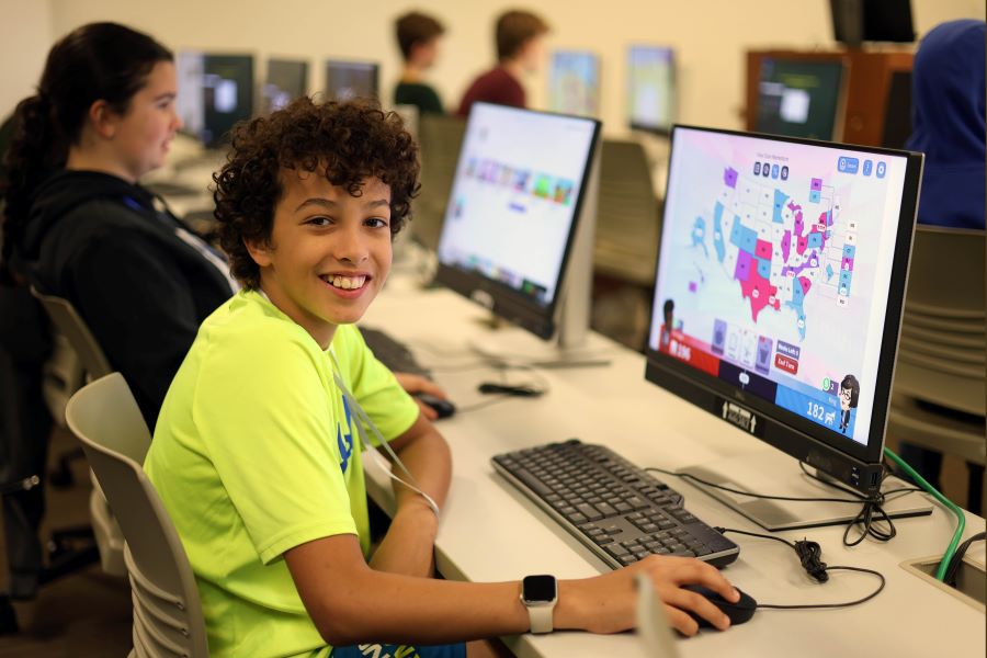 Smiling student playing online civics games on a computer.