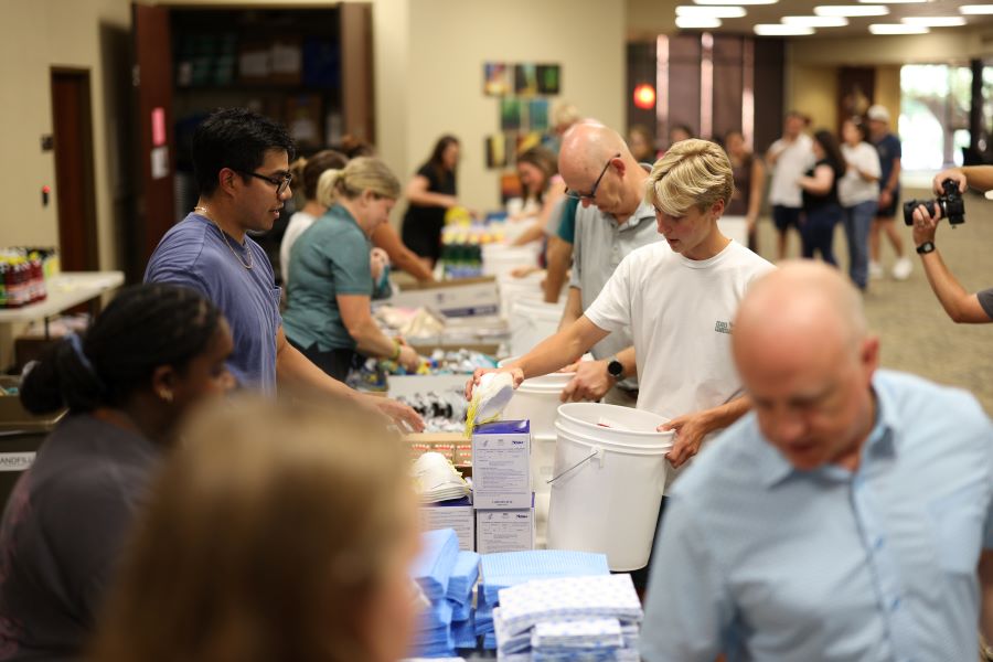 Baylor students, faculty and staff pick up supplies on tables to pack into disaster relief kits.