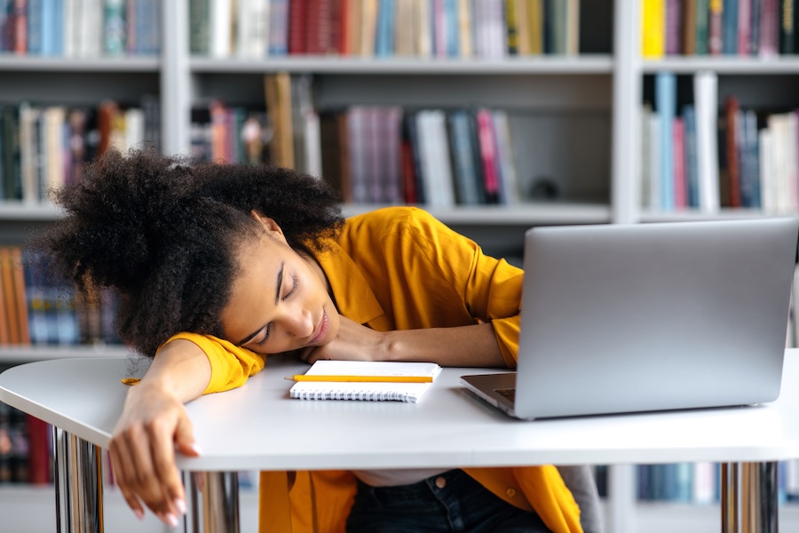 A tired sleepy African American female student fell asleep at a table during a lecture at a college