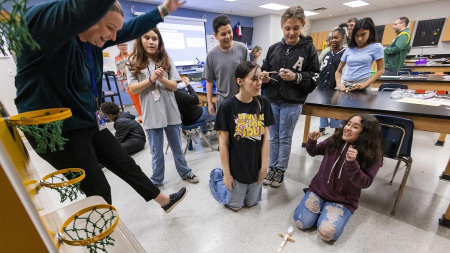 Students cheer as the catapult they built hits the basketball goal-type target.