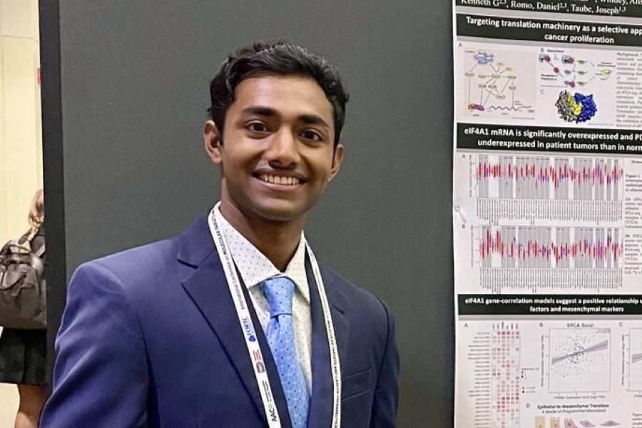 student in a suit and tie standing next to his research poster presentation