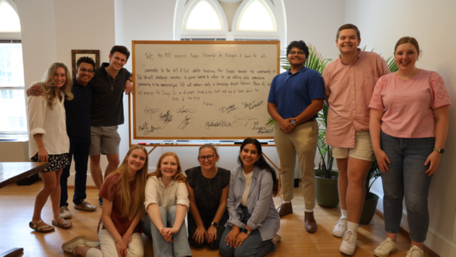 Group of students standing and sitting around a board with writing on it