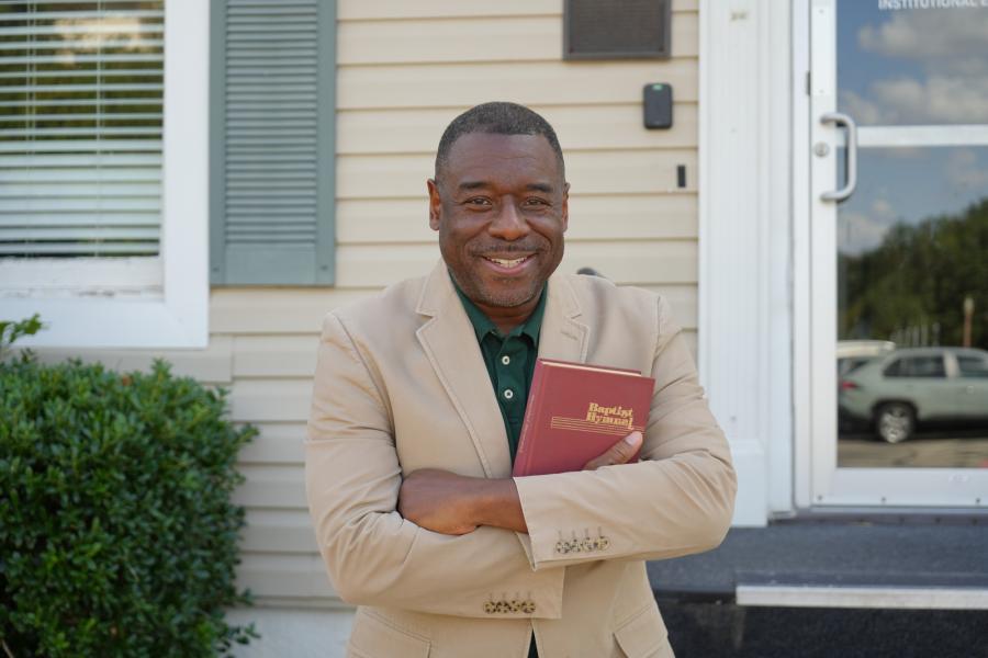 Stephen Newby holds a Baptist Hymnal before a historic building