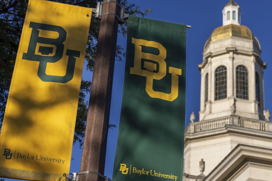 Gold and green Baylor lamppost flags with the tower of Pat Neff Hall in the background