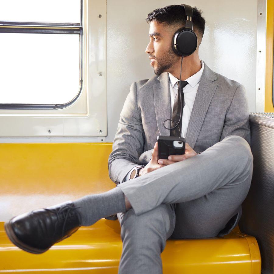 Young businessman wearing headphones and using a cellphone while staring out the window on a train during his commute