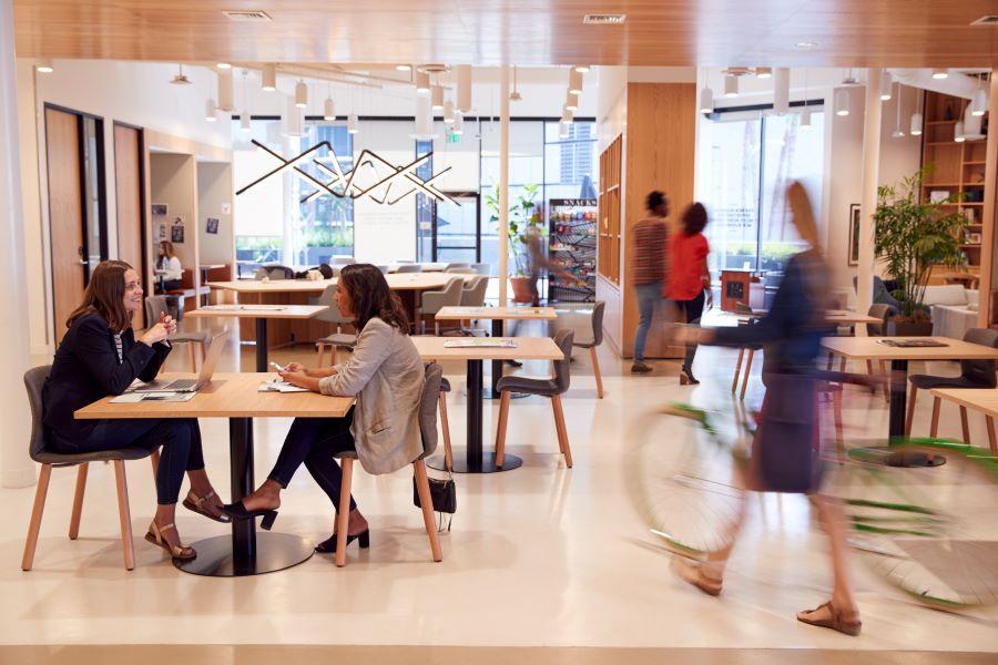 Interior Of Modern Open Plan Office With People Working And Commuters Arriving On Bikes