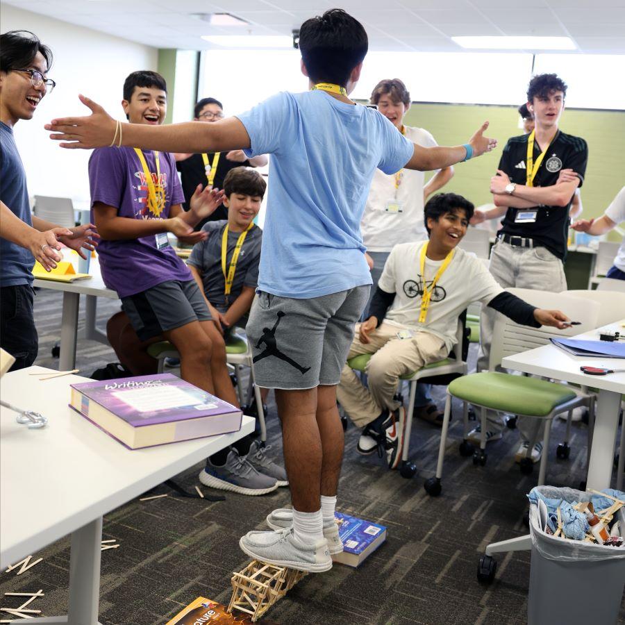 High school engineering student stands on a bridge made of popsicle sticks