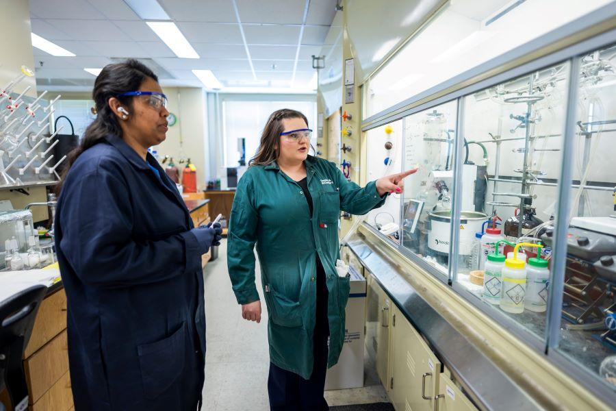 Baylor Chemistry Professor Liela Romero in her green lab coat working with a graduate student in her chemistry lab.