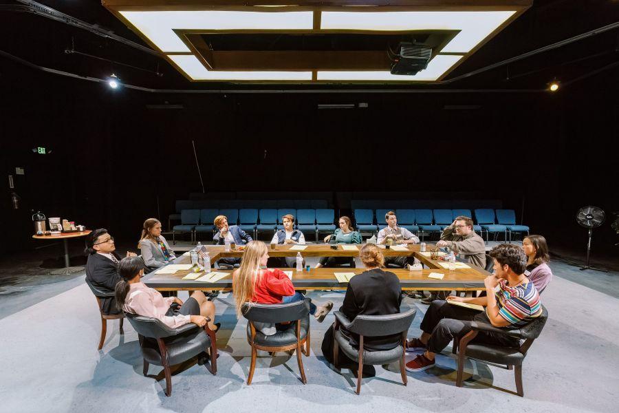 Twelve people sitting in chairs around a large table in a theater setting