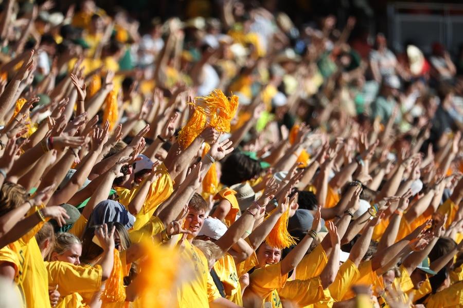Excited students cheer in the stands during a football game.