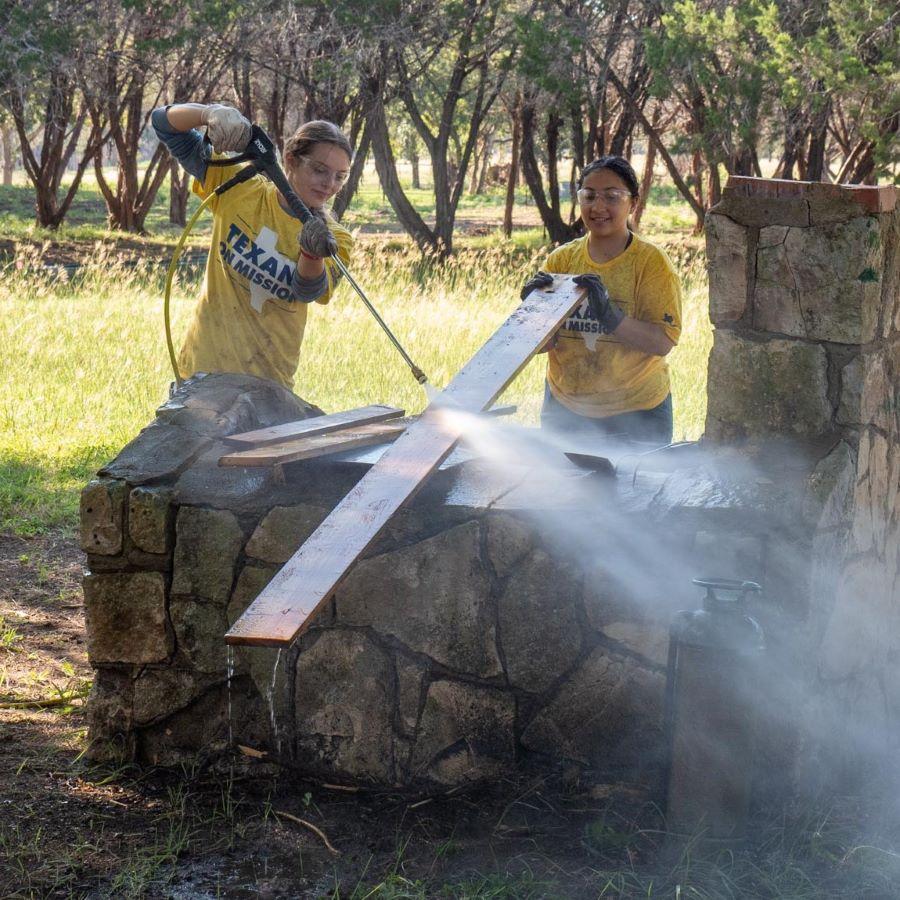 Two students in yellow Texans on Mission shirts powerwash a board