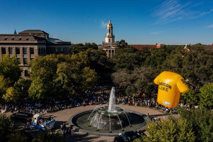 Crowds of people around a fountain along a parade route on a college campus.