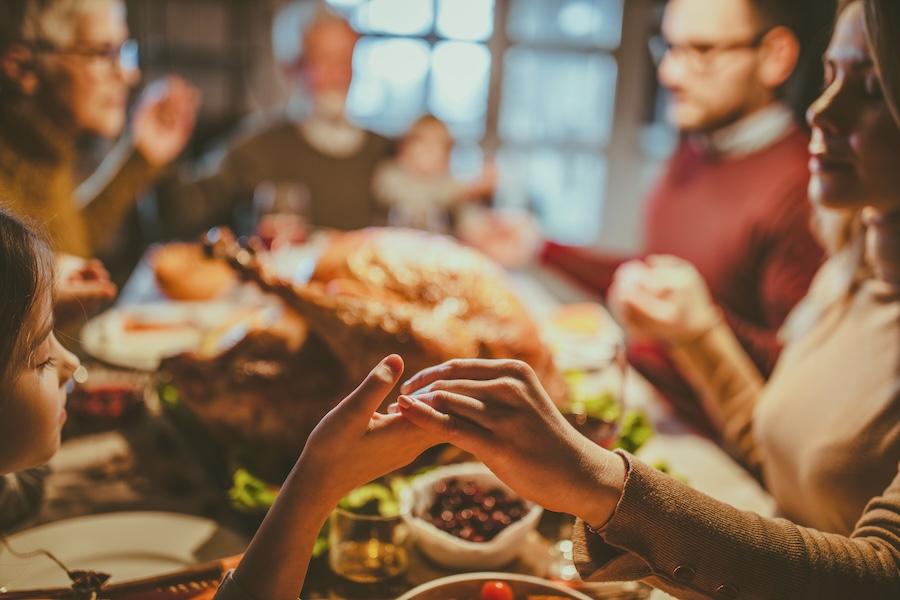 Close up of a mother and daughter holding hands while saying grace before family's Thanksgiving meal at dining room.