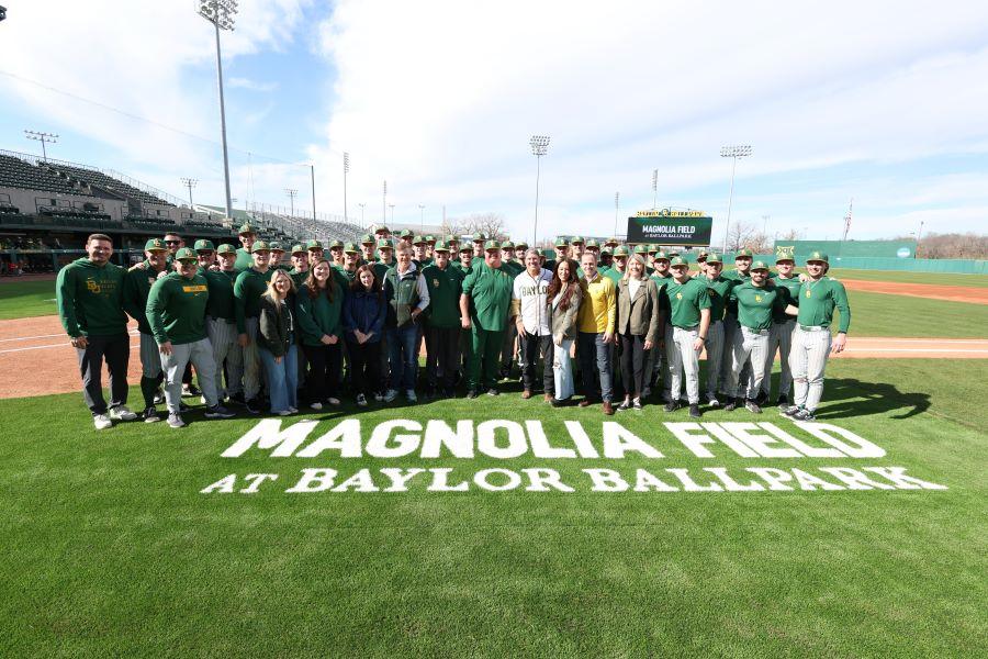 Group of people, including Chip and Joanna Gaines, stand together with the Baylor Baseball and Magnolia teams at Magnolia Field at Baylor Ballpark.
