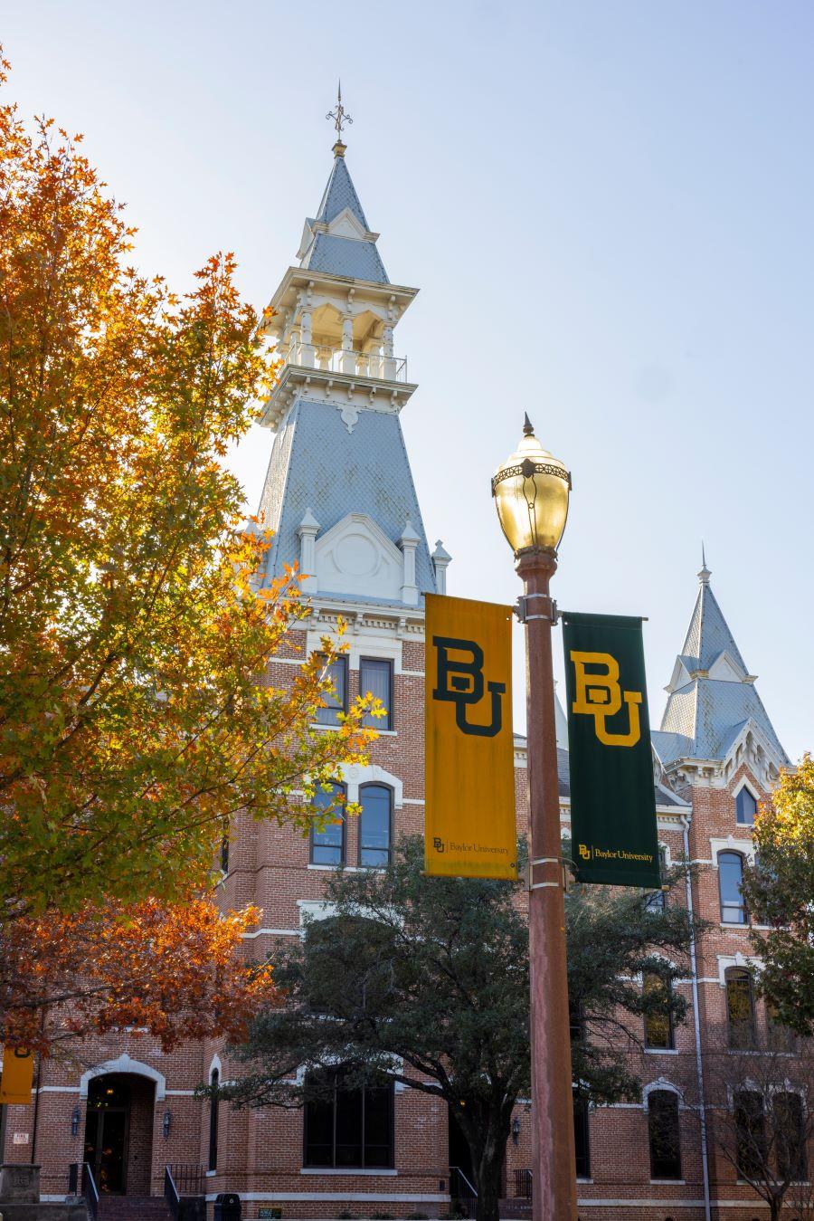 Spires atop Old Main, lampposts with green and gold interlocking BU's and trees in fall colors