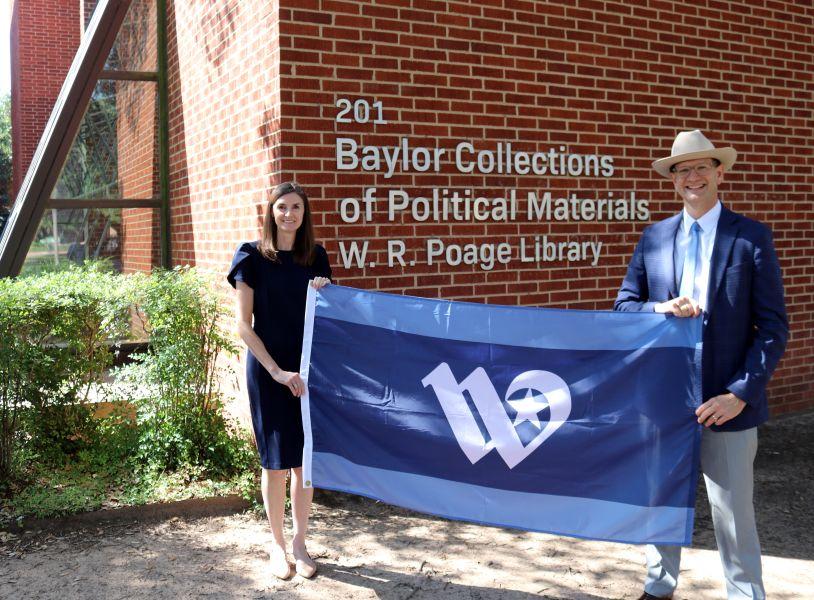 Jennifer and Josh Borderud hold a City of Waco flag in front of the Baylor Collections of Political Materials building