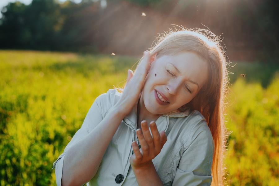  Young woman tries to kill a mosquito on her cheek - stock photo