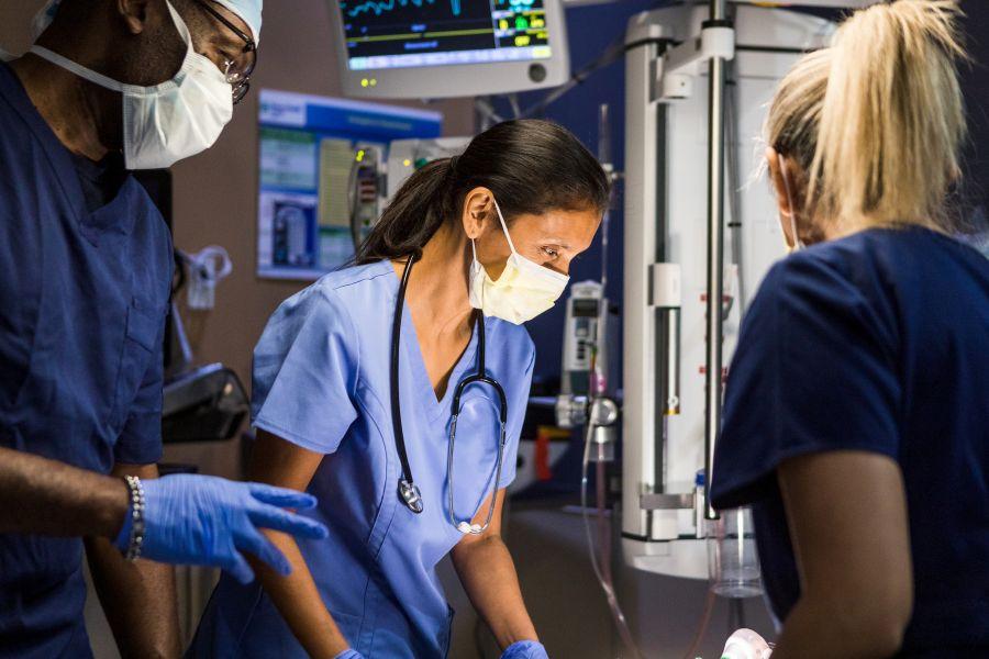 Diverse medical team evaluates unseen patient in darkened hospital room 
