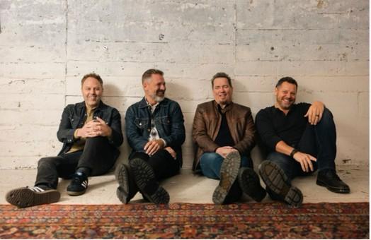 Four members of the Christian rock band Third Day smile while sitting by a brick wall.