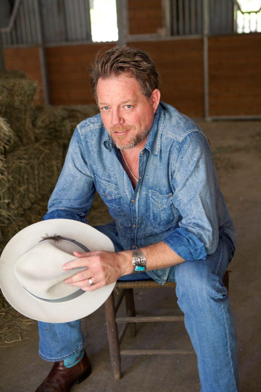 Texas country singer Pat Green sitting on a chair in a barn holding a white hat