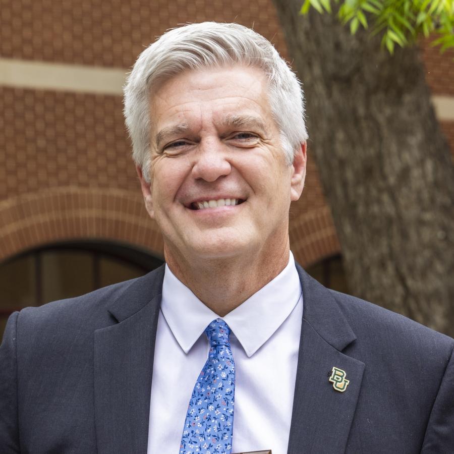 Baylor University history professor Stephen Sloan in a dark gray suit coat with a B-U lapel pin, white shirt and blue tie
