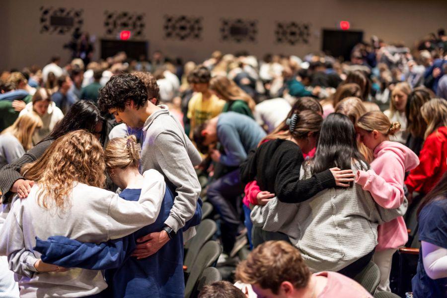 Students praying together in groups in a large auditorium