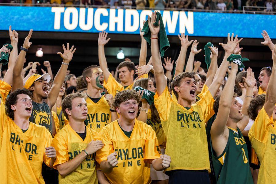 Students wearing gold Baylor Line jerseys celebrate a touchdown at a Baylor football game.